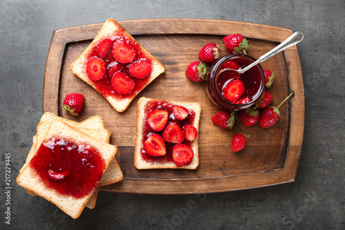 Board with slices of bread and delicious strawberry jam on dark table