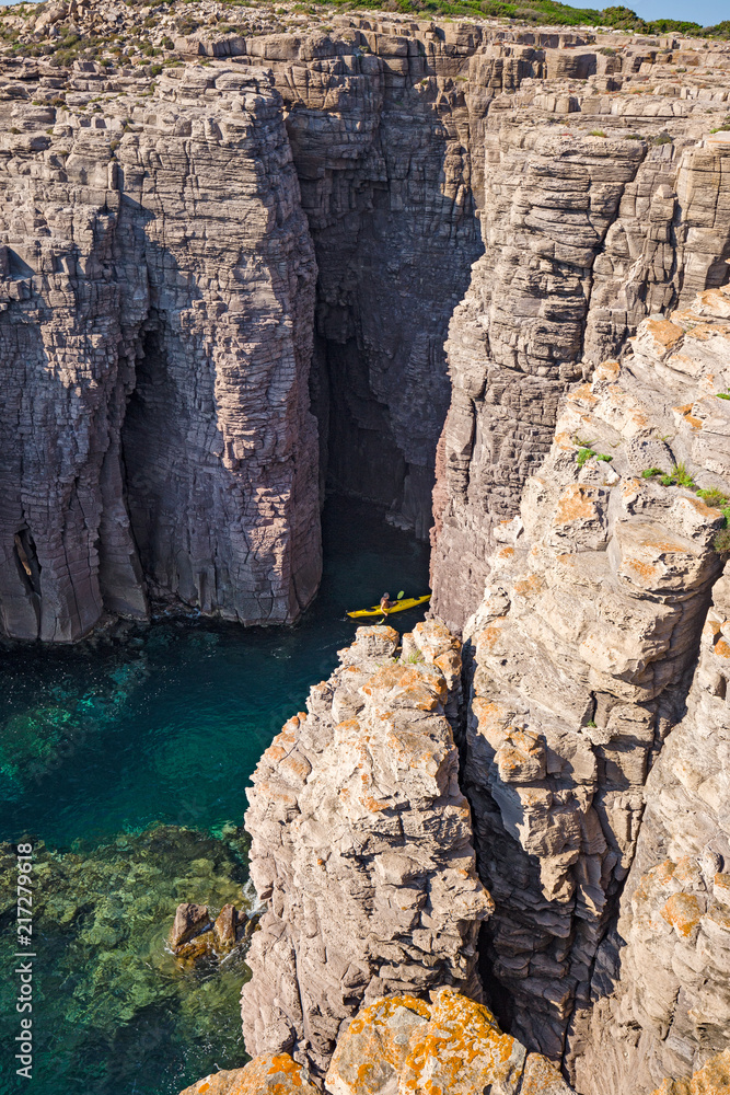 A canoe bather visits the caves between the rock formations of the cliffs of the island of San Pietro in Sardinia, Italy.