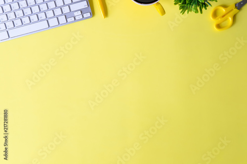 Office desk with computer keyboard, notebook paper, pen, coffee and plant decoration on yellow background top view mock up.