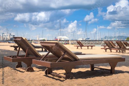 Fotografía Sun loungers on the sandy beach near the sea and marina