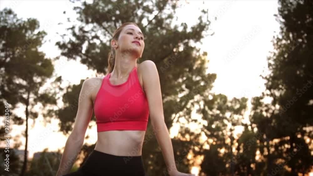 Medium shot of a beautiful young fit caucasian woman outside in her yoga outfit expressing confidence and determination. The background shows a morning sunshine through the trees. Slow Motion. Medium shot of a beautiful young fit caucasian woman outside in her yoga outfit expressing confidence and determination. The background shows a morning sunshine through the trees. Slow Motion.