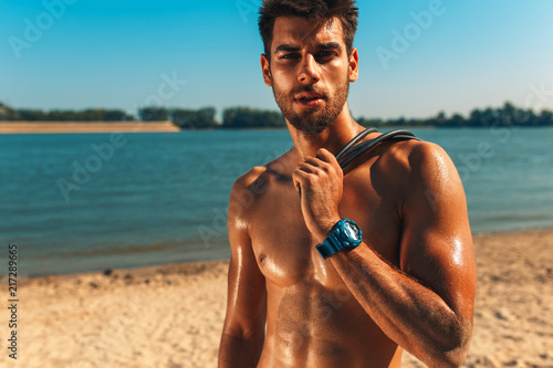 Portrait of young man resting after fitness workout at a beach on a sunny day.