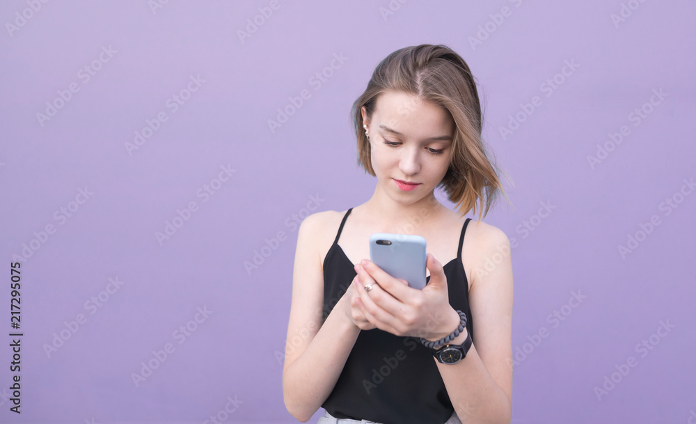 Attractive girl uses a smartphone on a pastel purple background. Portrait of a beautiful girl who is focused on a smartphone Attractive girl uses a smartphone on a pastel purple background. Portrait of a beautiful girl who is focused on a smartphone