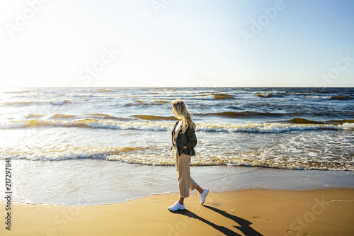 Photo side view of young woman in stylish clothing walking on seashore on summer day
