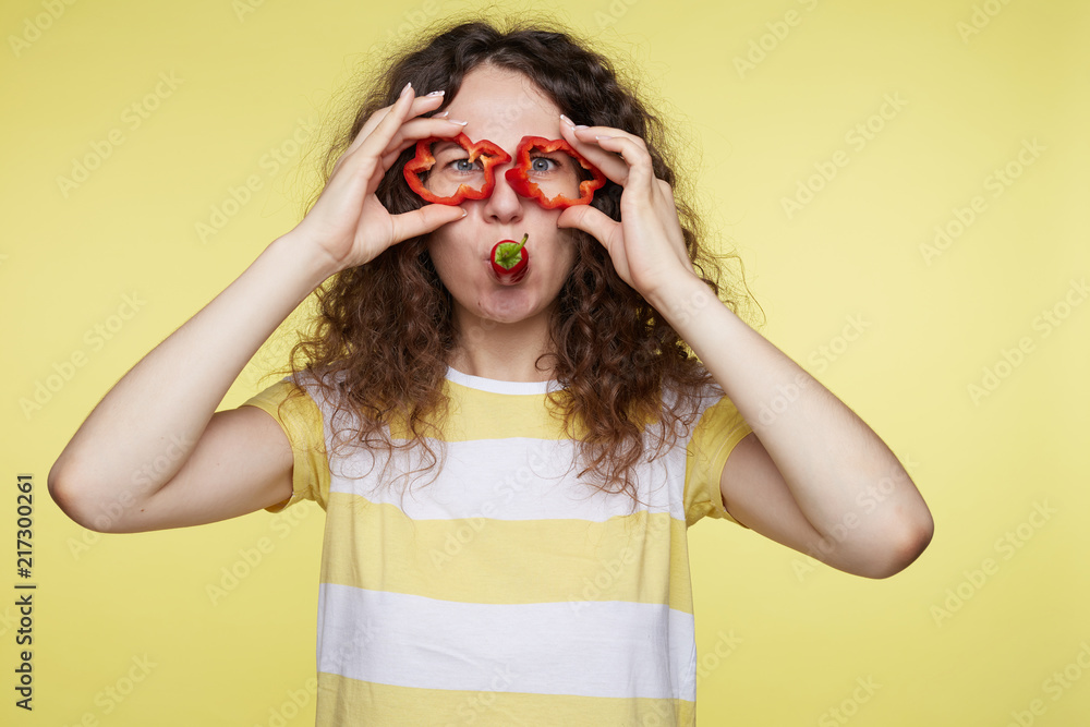 Young pretty lady with gorgeous smile and bushy hairstyle having fun indoors isolated over yellow studio background. Cute Caucasian woman playing with food while preparing dinner for great home party Young pretty lady with gorgeous smile and bushy hairstyle having fun indoors isolated over yellow studio background. Cute Caucasian woman playing with food while preparing dinner for great home party