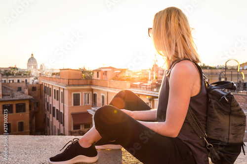 Fashinable female tourist with vintage hipster backpack admiring the beautiful view of at Piazza di Spagna, landmark square with Spanish steps in Rome, Italy at sunset.