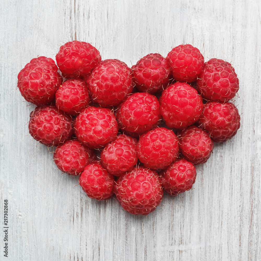 Raspberry close-up folded in the form of a heart on a white wooden board. Raspberry close-up folded in the form of a heart on a white wooden board.