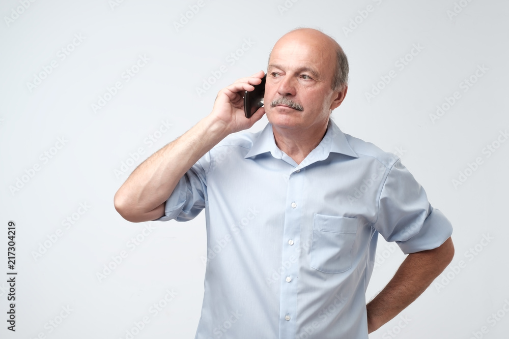 Serious, worried, upset mature man talking on cellphone Serious, worried, upset mature man talking on cellphone