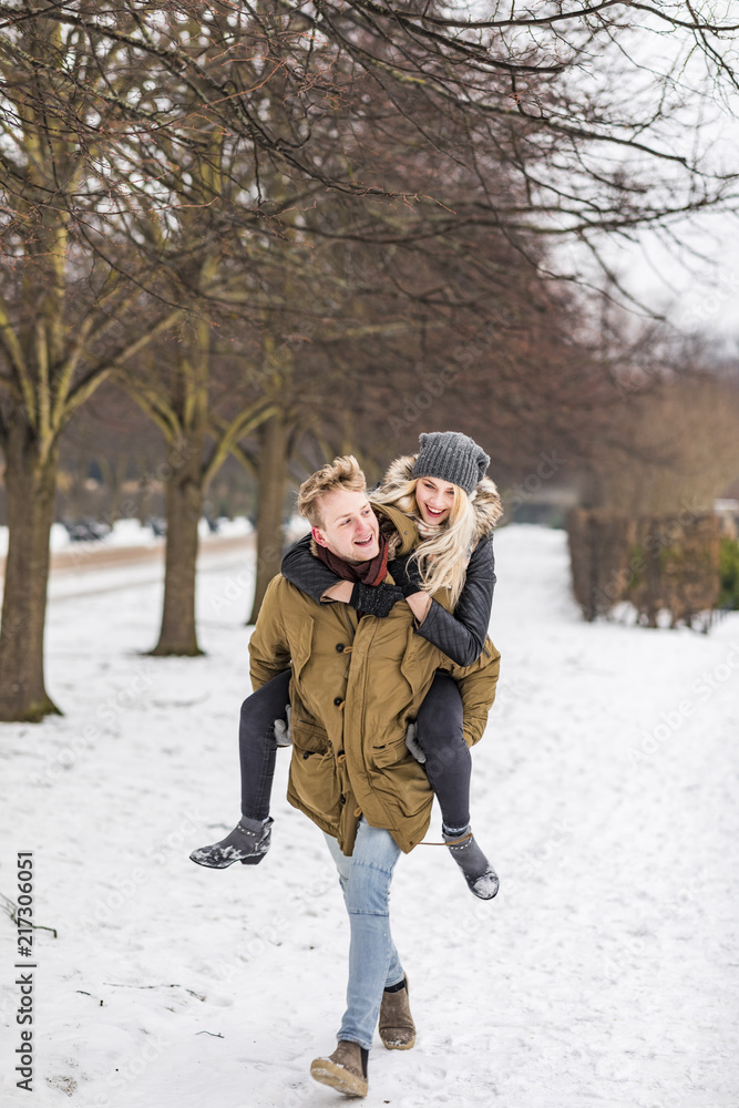 Young man giving his girlfriend a piggyback ride in winter Young man giving his girlfriend a piggyback ride in winter