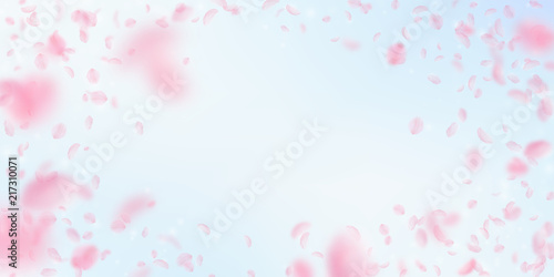 Sakura petals falling down. Romantic pink flowers vignette. Flying petals on blue sky wide backgroun