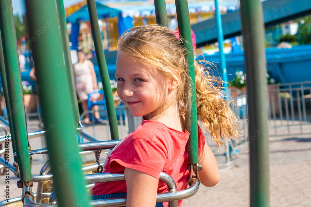 A happy and joyful girl sits on a swing, on a carousel and looks at the camera. A happy and joyful girl sits on a swing, on a carousel and looks at the camera.