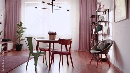 Video of a curtain moving in a pink dining room interior with a table, chairs, lamp, window and armchair