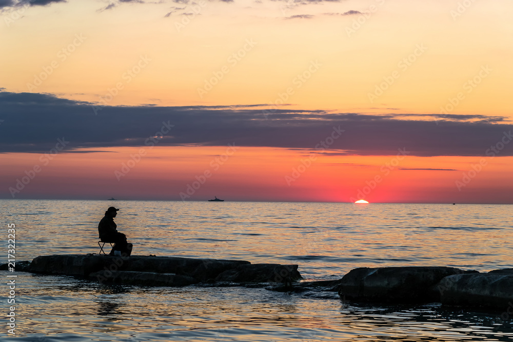lonely fisherman on a stone beach on a sunset background lonely fisherman on a stone beach on a sunset background