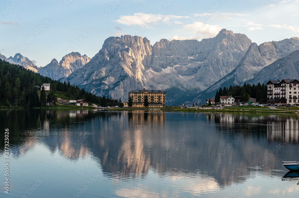 Buildings along the shoreline are reflected in the calm waters of Lake Misurina in the Italian Dolomites, just before sunset.