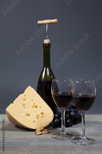 Bottle red wine and wine glasses, cheese and grape on wooden table