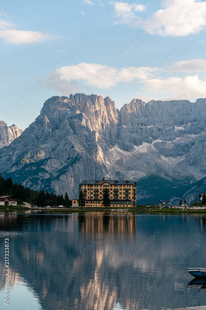 Fototapeta premium Buildings along the shoreline are reflected in the calm waters of Lake Misurina in the Italian Dolomites, just before sunset.
