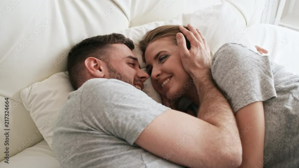 Handheld shot of happy bearded man and beautiful young woman lying on ...