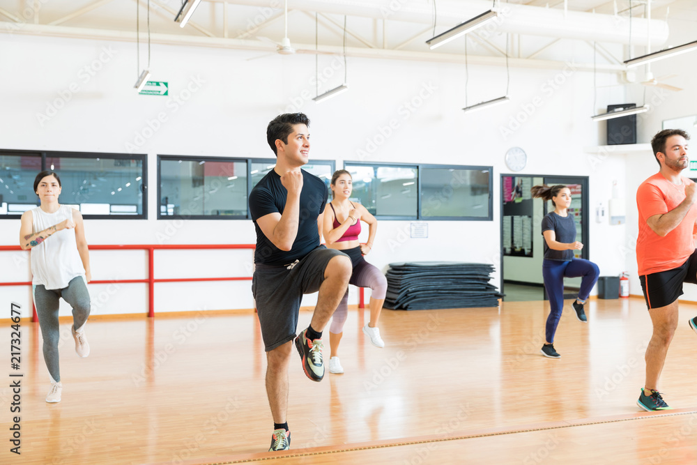 Fototapeta premium Man With Friends Performing High Knee Running In Aerobics Class