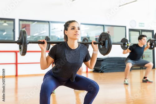 Female Client Exercising With Barbell In Health Club