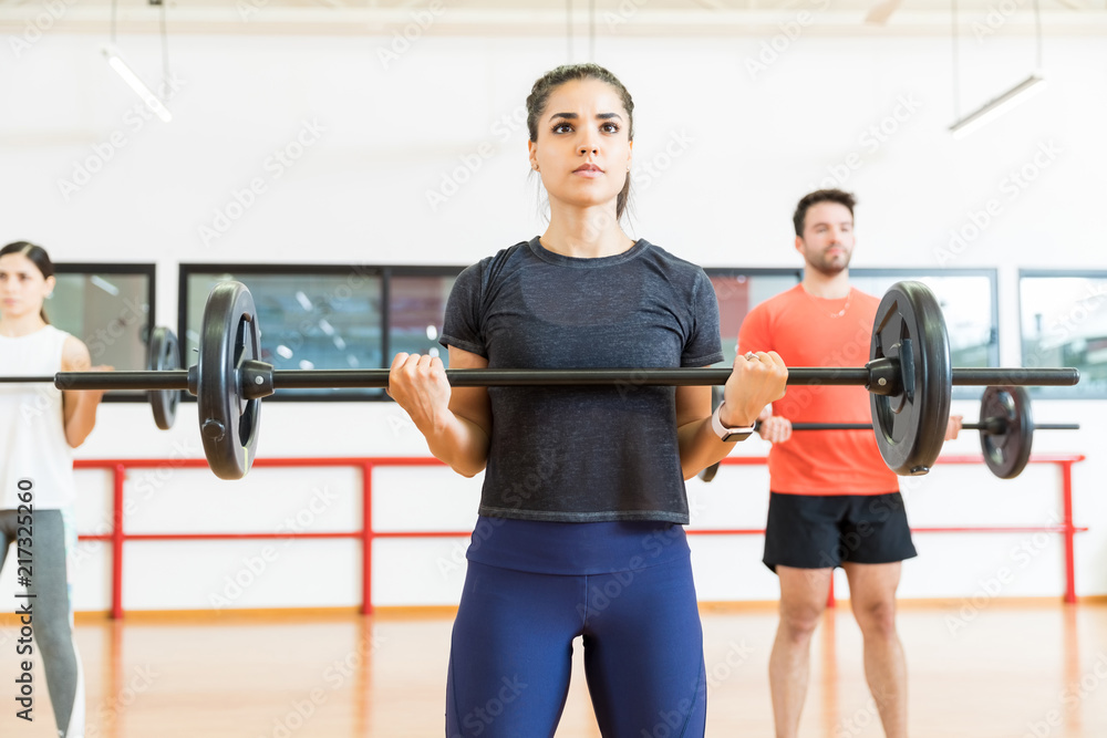 Fototapeta premium Female Practicing Weight Training With Friends In Gym