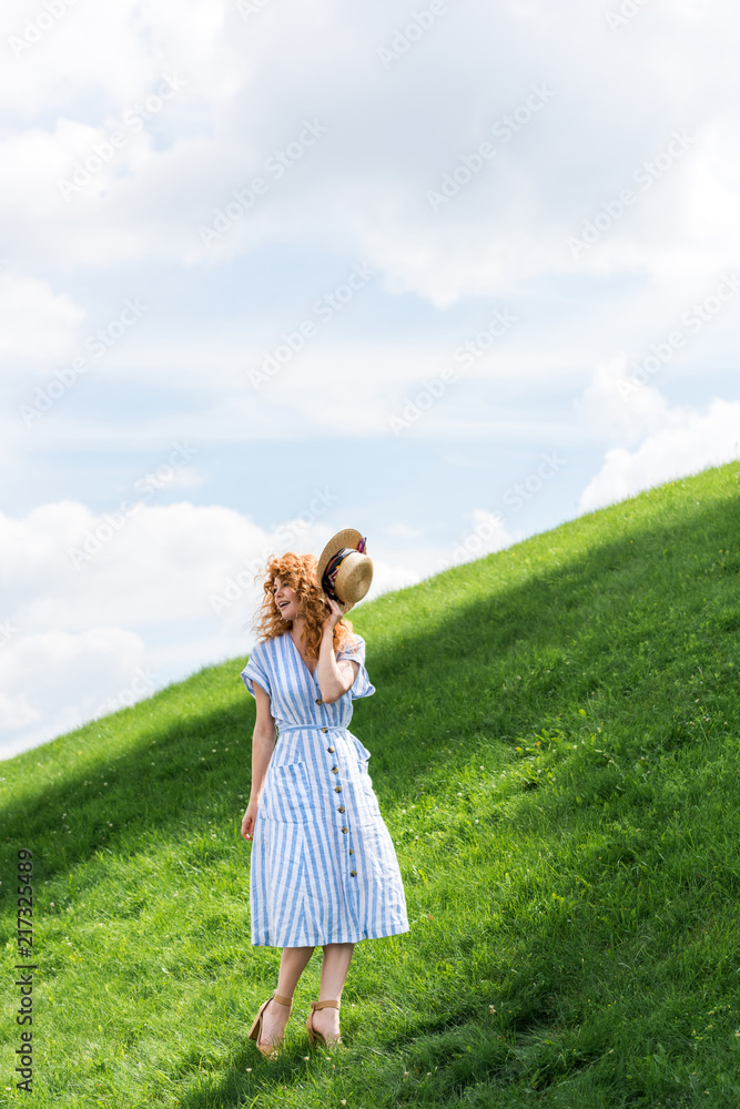 beautiful redhead woman holding straw hat on grassy hill beautiful redhead woman holding straw hat on grassy hill