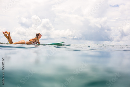 Canvas Print Beautiful young surfer woman in sexy pink bikini paddle surfing longboard on big waves in open ocean