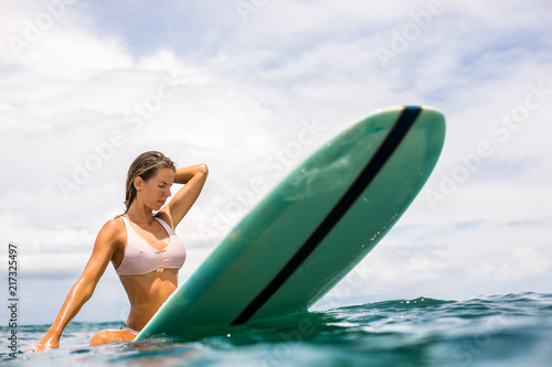 Fit beautiful young surfer girl in sexy pink bikini sit on surfing longboard in the open ocean. Modern family lifestyle, people water sport adventure camp and extreme swim on summer vacation.