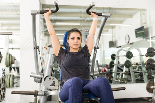 Serious Female Client Doing Shoulder Press In Health Club
