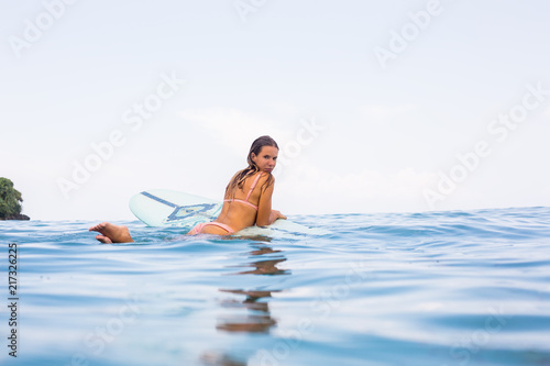 Beautiful surfer lady in sexy pink bikini rest in ocean water on surfing longboard. Girl have fun during hot summer day at tropic island resort, relax vacation concept. Hipster lifestyle advertising.