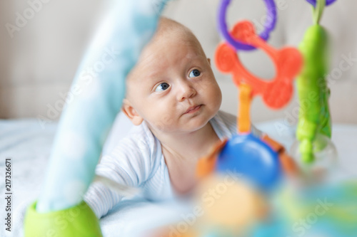 Charming baby in blue body, lies on the tummy and looks at the developing mat 