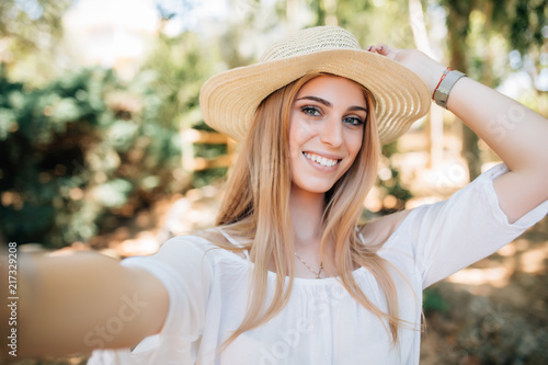 Portrait of happy woman wearing straw hat making selfie taking picture of herself in summer morning outdoors .