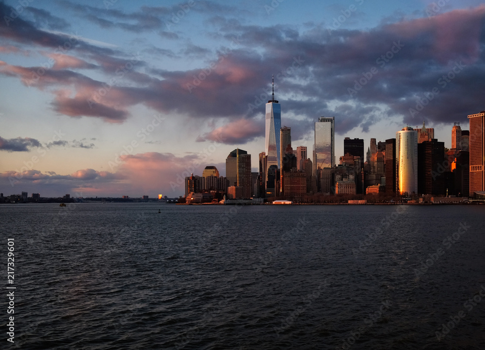 New York City skyline with urban skyscrapers over Hudson River at sunset. Manhattan downtown panorama. Waterfront view to the harbor at twilight.

