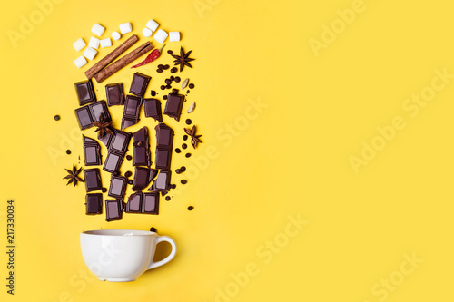 Hot chocolate cup, chocolate pieces, spices and marshmallows on yellow background