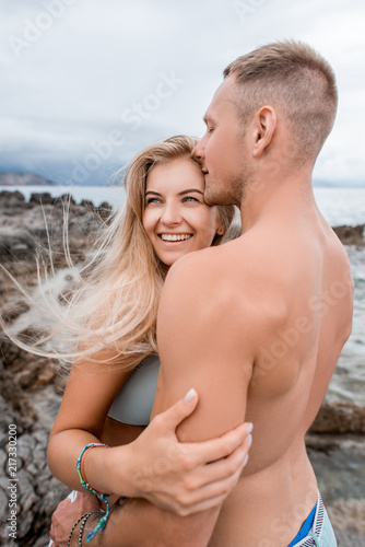 young muscular man hugging and kissing happy girlfriend on rocky beach in montenegro