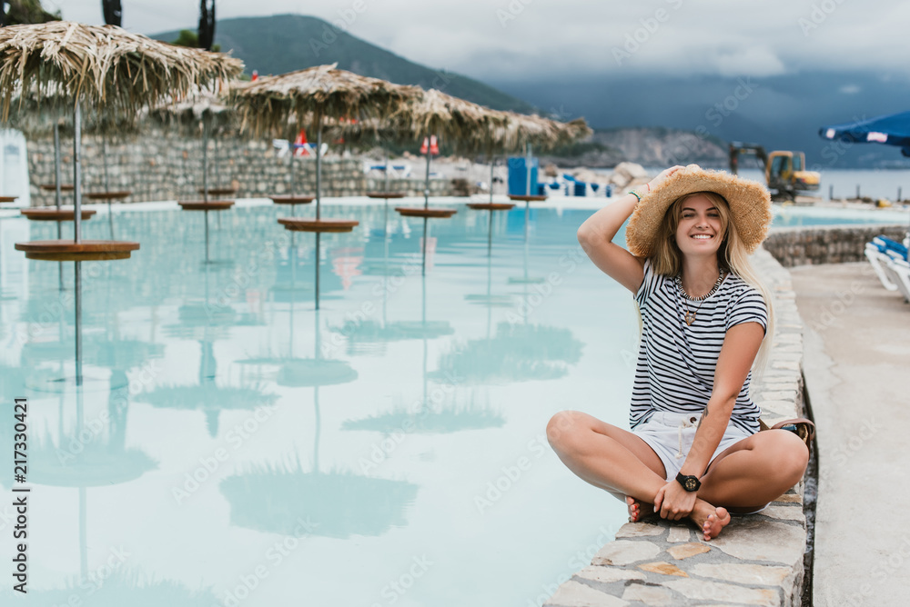 beautiful happy young woman in straw hat sitting near pool and smiling at camera, montenegro