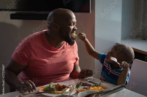 Son feeding his father breakfast on dinning table photo