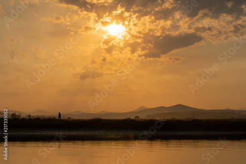 hiker at sunrise in front of water with clouds