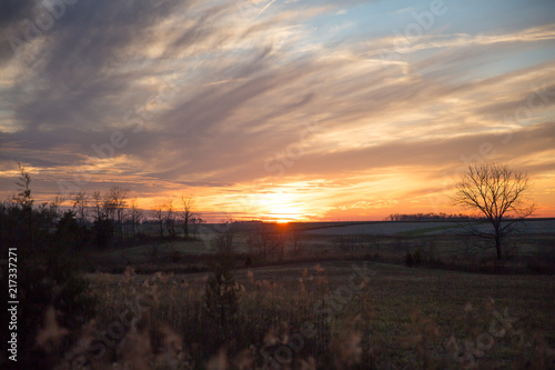 Cloudy Winter Sunset over Wild Grass and Fields with Blue Sky in Blurred Foreground.