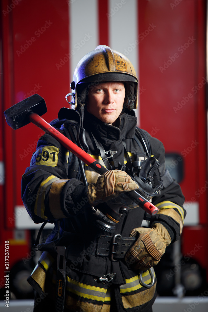 Photo of fireman with sledgehammer in hands near fire engine Photo of fireman with sledgehammer in hands near fire engine