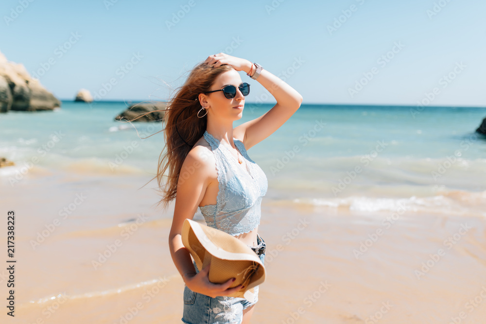 Young woman in sunglasses walking along the beach in sunny day Young woman in sunglasses walking along the beach in sunny day