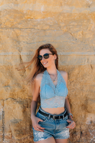 Young beauty woman in sunglasses posing on the beach in front of cliff background photo