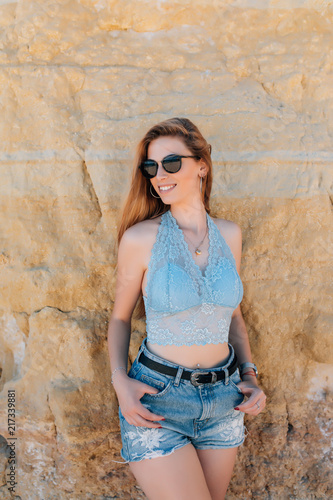 Portrait of attractive blonde girl in sunglasses posing on rocky beach on sunset background. © dianagrytsku