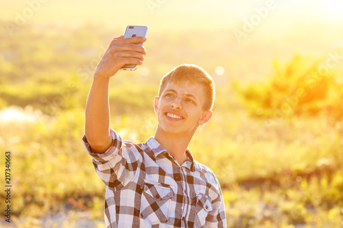 happy young man doing a selfie on the phone and smiling, natural background in the sunlight