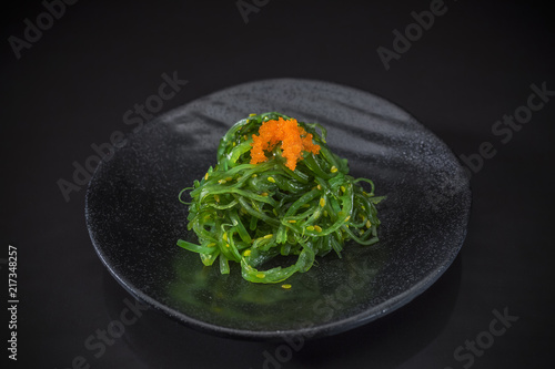 Wakame Sashimi, wakame salad served on traditional Japanese food on ceramic dish, Japanese food style, Japanese menu, wakame seaweed salad toped with shrimp eggs on black background, selective focus