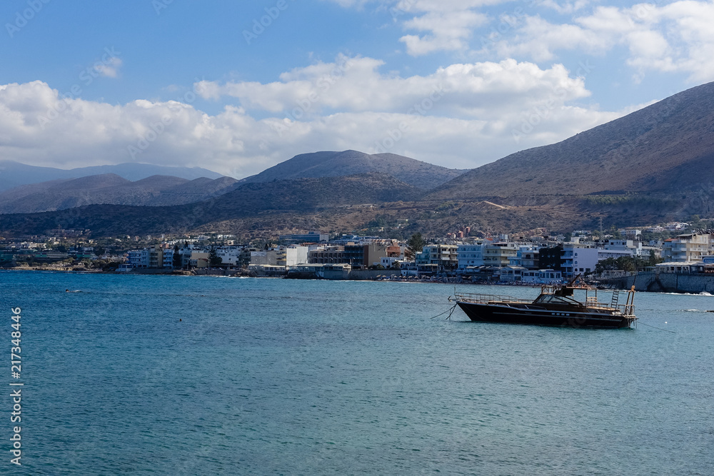 a small village on the shores of the Mediterranean Sea; mountains are visible in the background, with sea by boat in the foreground; Sea view with mountains and blue sky with white clouds