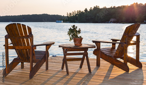 Chairs on a deck overlooking a lake at sunset.