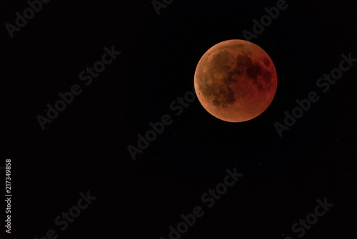 a full moon or blood moon during a complete lunar eclipse in a black night sky with stars