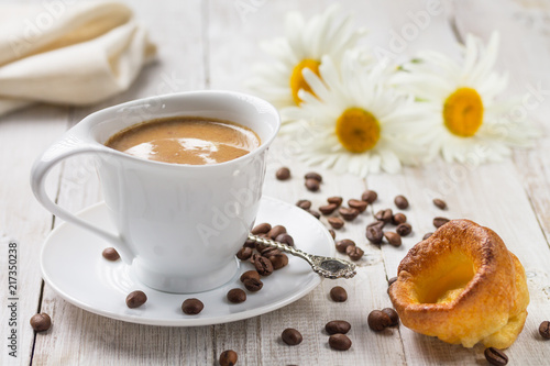 A cup of hot coffee with yorkshire pudding and daisies on a white wooden background. Breakfast