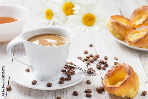 A cup of hot coffee with yorkshire puddings and daisies on a white wooden table. Breakfast