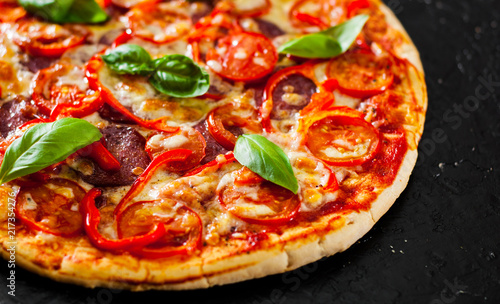 Pizza with Mozzarella cheese, Ham, Tomatoes, salami, pepper, pepperoni Spices and Fresh Basil. Italian pizza.on black background